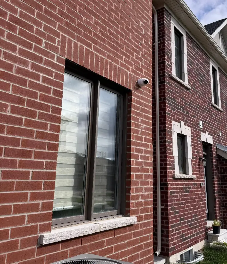 4K dome camera mounted on the side of a red brick Durham home between windows, clean conduit run, residential install.