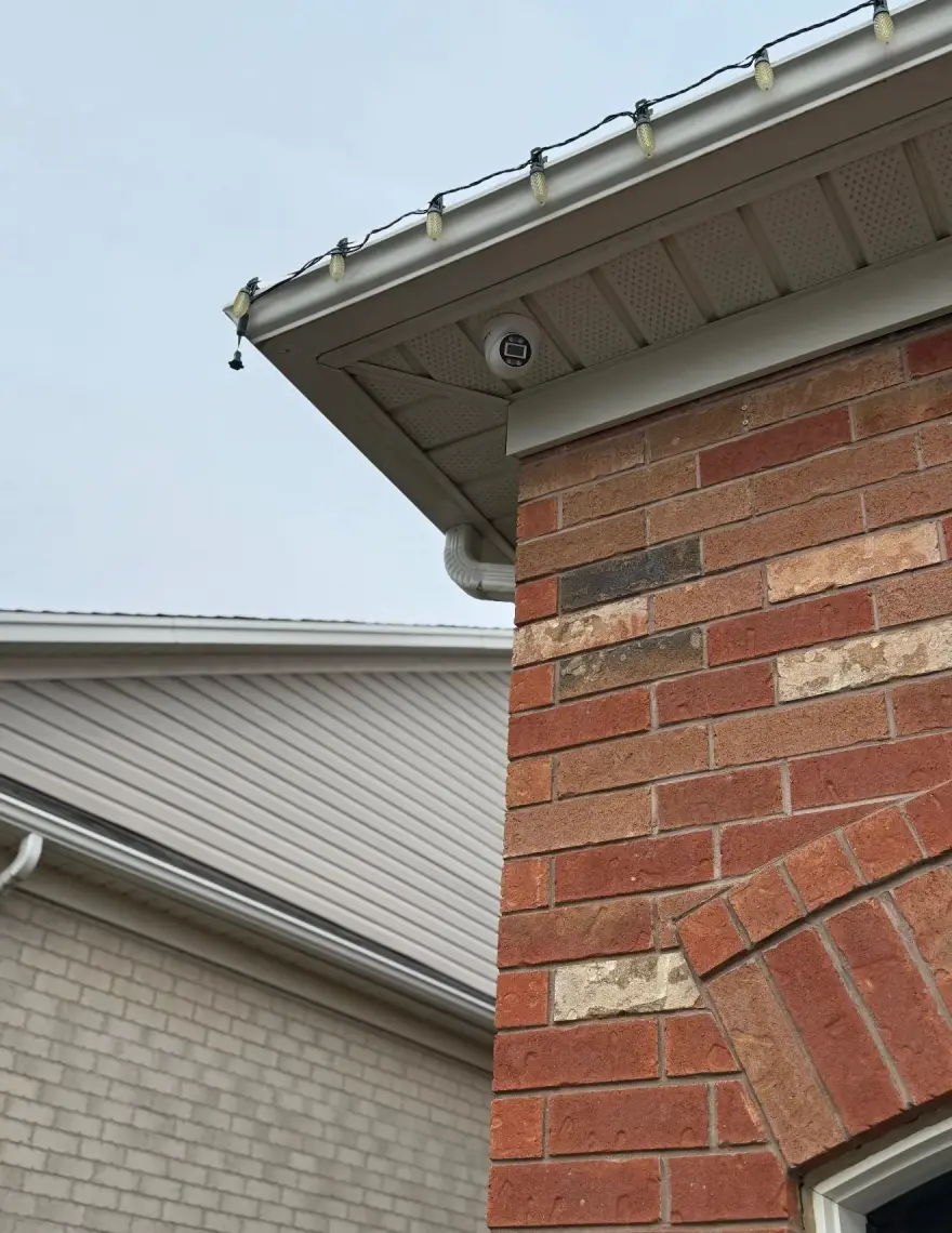 4K dome camera mounted in the soffit corner of a Durham brick home, positioned to cover the full property edge.